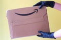 Hands in black protective gloves receiving Amazon Prime package delivered. Yellow background. copy space