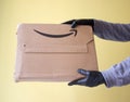 Hands in black protective gloves receiving Amazon Prime package delivered. Yellow background. copy space