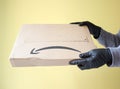 Hands in black protective gloves receiving Amazon Prime package delivered. Yellow background. copy space