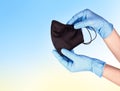 Hands in blue disposable medical gloves holding black respiratory facial mask. Pandemic corona virus, Royalty Free Stock Photo