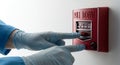 Hands in Blue Gloves Activate Red Fire Alarm Pull Station on White Wall Pull Down Handle for Emergency with Protective Gloves in Royalty Free Stock Photo
