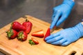 Hands in blue gloves cut red strawberries on a wooden Board for fruit salad. Royalty Free Stock Photo