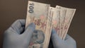Hands with blue protective medical gloves are counting 100 hundred Turkish Lira