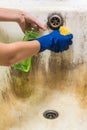 Hands in blue rubber worker handgloves hold sponge and spray with cleaning liquid trying to wash bath tub Royalty Free Stock Photo