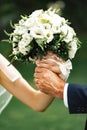 Hands of the bride and groom intertwined and hold a wedding bouquet of delicate white roses, eustomas. Close-up. Hands of the Royalty Free Stock Photo