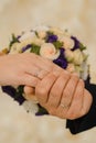 Hands of the bride and groom with wedding rings on the background of a delicate bouquet.
