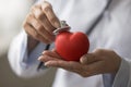 Hands of cardiologist applying stethoscope to red heart shaped object