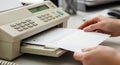 Close-up of hands feeding a document into an older model office beige fax machine Royalty Free Stock Photo