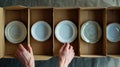 hands carefully stacking plates into a cardboard moving box, illustrating the meticulous process of packing and securing