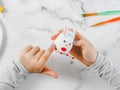 Hands of a caucasian girl in a gray turtleneck holding an easter bunny egg and sticking a colored sticker