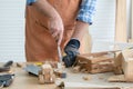 Hands of Caucasian senior old man carpenter in apron and glove using chisel working in workshop, tools machine small wooden toy Royalty Free Stock Photo