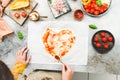 Hands of a caucasian teenage girl in an apron smear tomato sauce on a heart-shaped pizza dough. Royalty Free Stock Photo