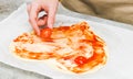 Hands of caucasian teenage girl lay down sliced cherry tomato on heart-shaped pizza dough. Royalty Free Stock Photo