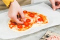 Hands of caucasian teenage girl lay down sliced cherry tomato on heart-shaped pizza dough. Royalty Free Stock Photo