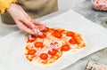 Hands of caucasian teenage girl lay down sliced cherry tomato on heart-shaped pizza dough. Royalty Free Stock Photo