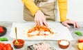 Hands of a Caucasian teenage girl smear a spoonful of pizza sauce on a heart-shaped dough. Royalty Free Stock Photo