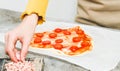 Hands of caucasian teenage girl take finely chopped ham for heart pizza dough.