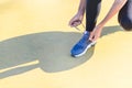 Hands of a caucasian woman tying her blue sport shoes and projecting a shadow on a yellow floor