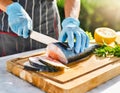 Hands of a chef in apron cutting fresh fish with knife on wooden cutting board