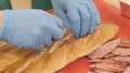 Hands chef cook putting pieces sausage in baguette in restaurant kitchen closeup