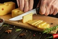 The hands of the chef with a knife cut milk cheese on a cutting wooden kitchen board. Cooking dairy products with pepper and Royalty Free Stock Photo