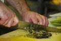 The hands of the chef with a large kitchen knife, sliced arugula salad