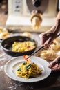 Hands of chef plating freshly cooked pasta with a pasta maker in the background