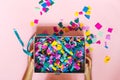 Children`s hands hold a gift box full of colorful confetti. Top view, horizontally on a pink background Royalty Free Stock Photo