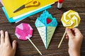 In the hands of a child origami paper ice cream and lollipop on a wooden table.