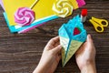 In the hands of a child origami paper ice cream on a wooden table.