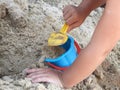 Hands of child playing in the sandbox with yellow scoop and blue bucket