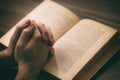 Hands clasped in prayer over a Holy Bible, wooden table background Royalty Free Stock Photo