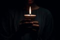 A hands close up in a dark room, surrounded by shadows, holding a single burning candle Royalty Free Stock Photo