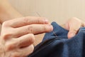 Hands of clothier sew jeans clothes with a needle closeup