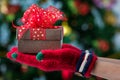 Hands in colorful red gloves holding give box with beautiful bow