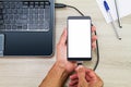 Hands connecting blank white screen smartphone to laptop by using usb cable on wooden desk with pen and paper Royalty Free Stock Photo