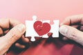 Hands connecting or disconnecting jigsaw puzzle pieces with red heart