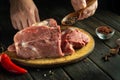 The hands of the cook add pepper to raw meat before grilling. Preparing beef meat before roasting. Working environment in kitchen Royalty Free Stock Photo