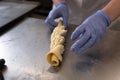 The hands of the cook in blue protective gloves are preparing a roll stuffed with cottage cheese and sugar. Manual production of