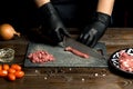 Hands of the cook in gloves cut the red meat on the board. nearby are tomatoes, onion, butter Royalty Free Stock Photo