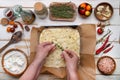 hands of the cook lay the dough for focaccia in a metal pan with spices. View from above