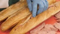 Hands cook putting pieces sausage in cut up baguette in fast food cafe