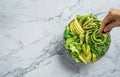 Hands cooking fresh summer salad with avocado, kiwi, apple, cucumber, pear, micro greens, lime and sesame on light marble