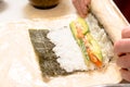 Hands cooking sushi with rice, salmon and nori