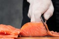 Hands cooks close-up. The chef cuts with a knife a red fish, smoked salmon on a wooden cutting board. Royalty Free Stock Photo