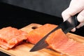 Hands cooks close-up. The chef cuts with a knife a red fish, smoked salmon on a wooden cutting board. Royalty Free Stock Photo