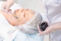 Hands of cosmetology specialist applying carbon nanogel on young woman patient face using brush, getting ready for