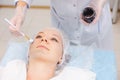 Hands of cosmetology specialist applying carbon nanogel on young woman patient face using brush, getting ready for