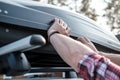 Hands cover the assembled, roomy trunk or cargo box on the roof of the car, before leaving for a family vacation.