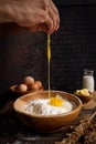 Hands cracking egg into a bowl of flour against dark background